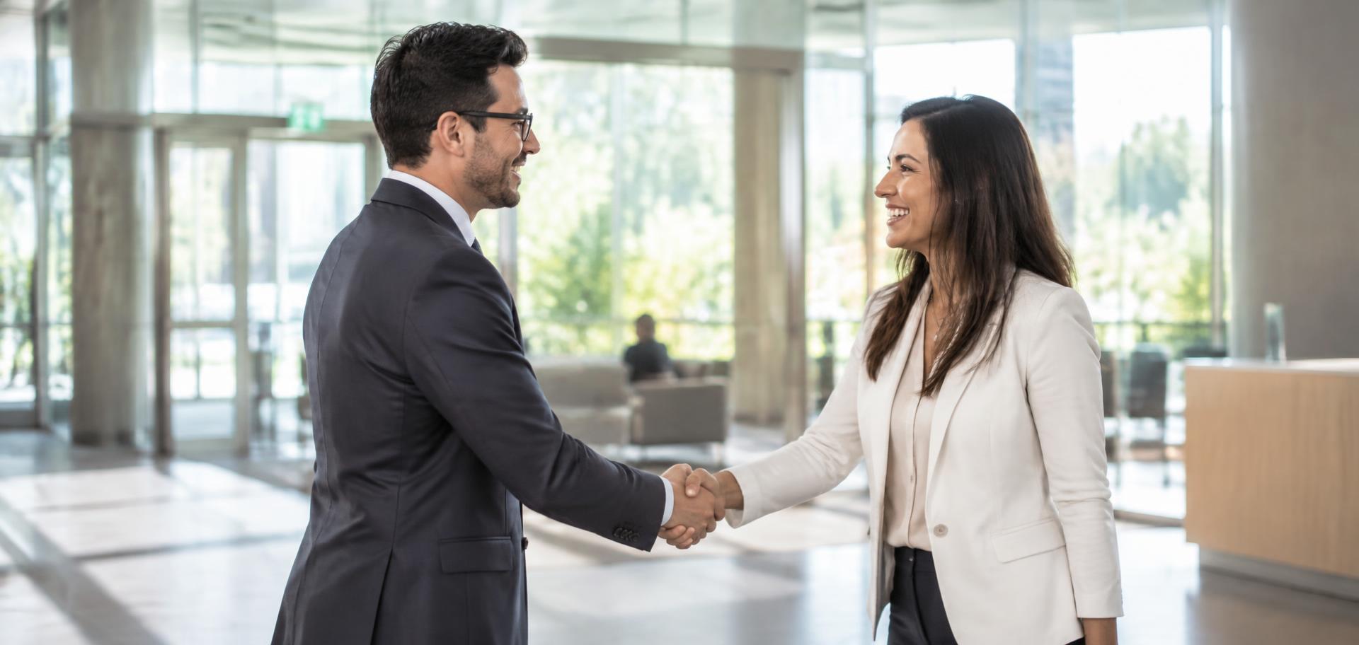 Two professionals shaking hands in a bright office lobby